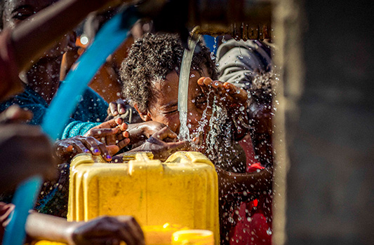 Happy kids filling a water can from a fresh water source